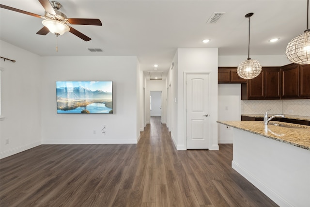 kitchen featuring light stone countertops, decorative light fixtures, dark brown cabinets, dark wood-type flooring, and decorative backsplash