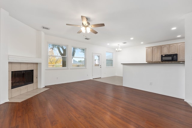 unfurnished living room with ceiling fan with notable chandelier, dark hardwood / wood-style flooring, and a tiled fireplace