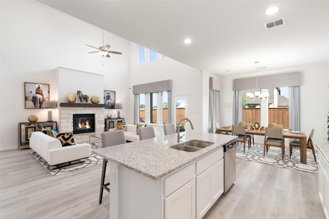 kitchen with sink, a kitchen island with sink, stainless steel dishwasher, white cabinetry, and a fireplace