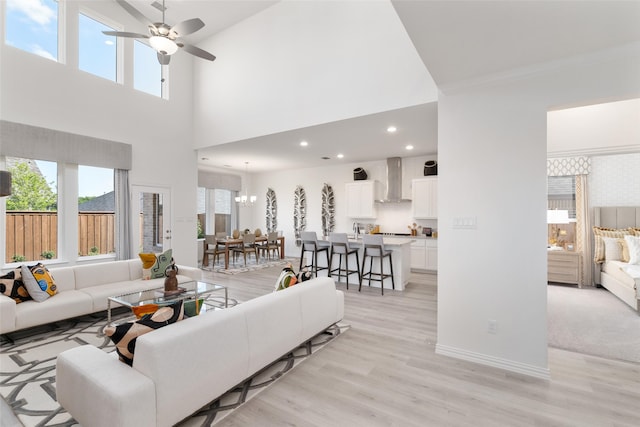 living room featuring a towering ceiling, ceiling fan with notable chandelier, and light hardwood / wood-style flooring