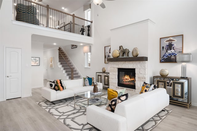 living room featuring ceiling fan, a towering ceiling, a stone fireplace, and light wood-type flooring