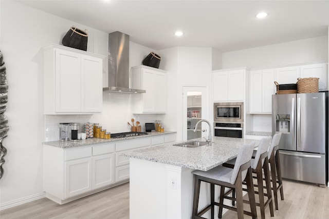 kitchen with stainless steel appliances, white cabinetry, sink, wall chimney exhaust hood, and a kitchen island with sink