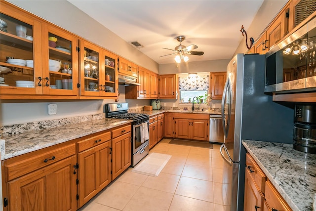 kitchen with appliances with stainless steel finishes, ceiling fan, sink, light stone counters, and light tile patterned floors