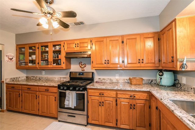 kitchen with stainless steel gas range oven, ceiling fan, light tile patterned flooring, light stone countertops, and sink