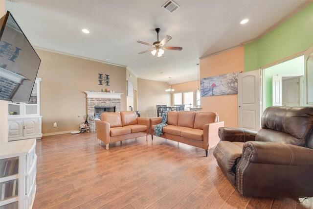 living room with a brick fireplace, ceiling fan, light hardwood / wood-style flooring, and ornamental molding