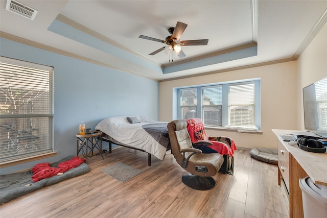 bedroom with crown molding, light wood-type flooring, ceiling fan, and a raised ceiling