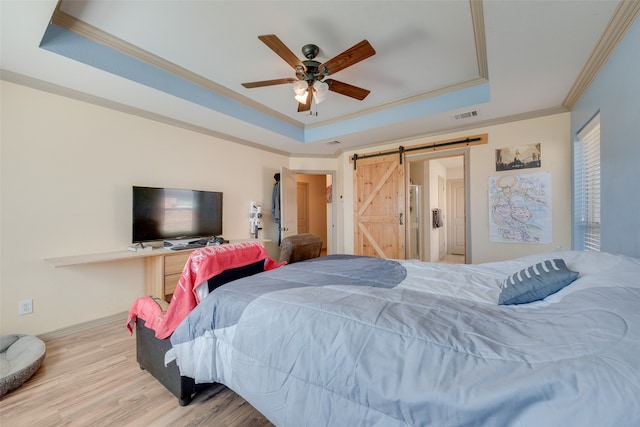 bedroom featuring a barn door, ornamental molding, ceiling fan, a raised ceiling, and light wood-type flooring