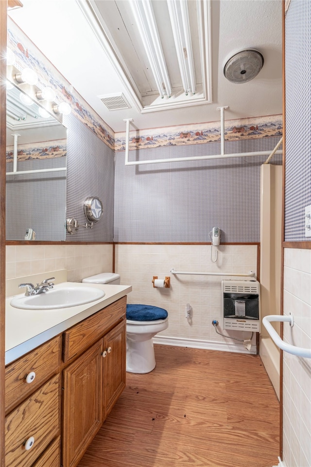 bathroom featuring heating unit, tile walls, hardwood / wood-style flooring, vanity, and toilet