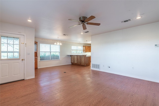 unfurnished living room with ceiling fan with notable chandelier and light wood-type flooring