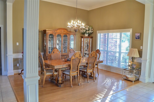 dining room with a high ceiling, ornamental molding, a notable chandelier, decorative columns, and light wood-type flooring