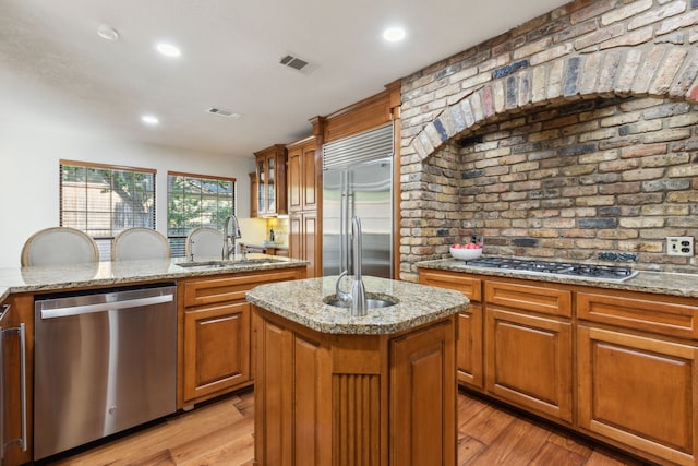 kitchen with light hardwood / wood-style floors, a center island with sink, sink, and appliances with stainless steel finishes