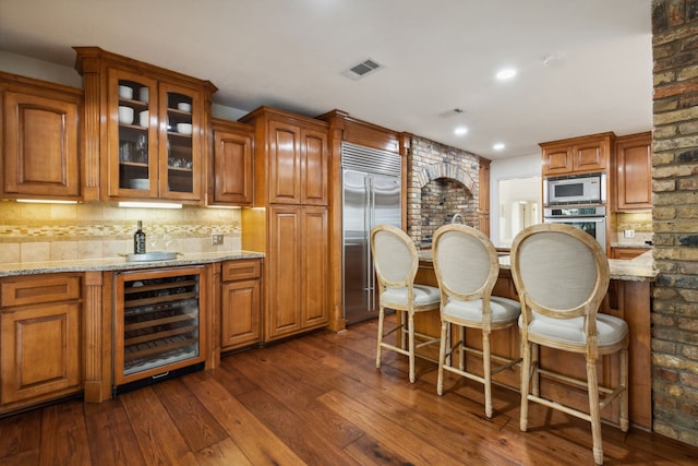 bar featuring dark wood-type flooring, beverage cooler, light stone countertops, and built in appliances