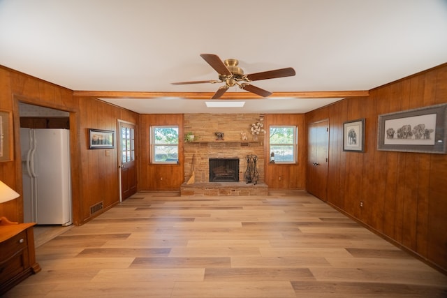 unfurnished living room featuring a fireplace, wood walls, ceiling fan, and light hardwood / wood-style flooring