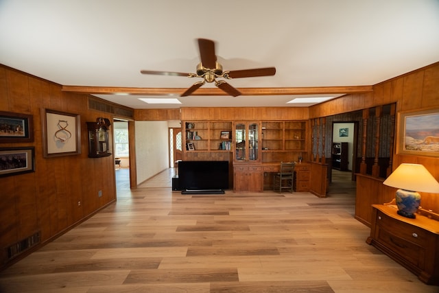 living room with ceiling fan, wooden walls, built in features, and light hardwood / wood-style flooring