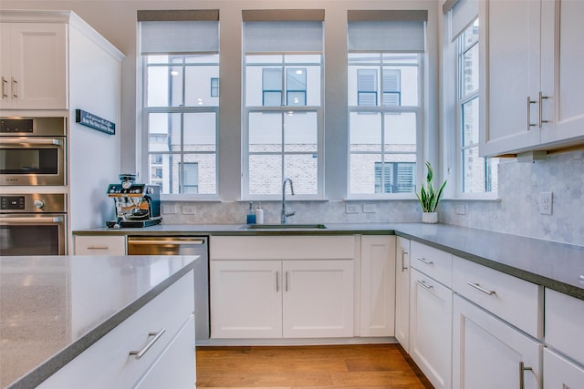 kitchen with light hardwood / wood-style flooring, stone countertops, appliances with stainless steel finishes, sink, and white cabinets