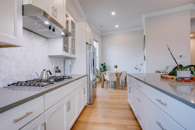 kitchen featuring white cabinets, appliances with stainless steel finishes, decorative backsplash, ornamental molding, and light wood-type flooring