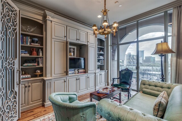 living room with built in features, light wood-type flooring, a notable chandelier, and crown molding