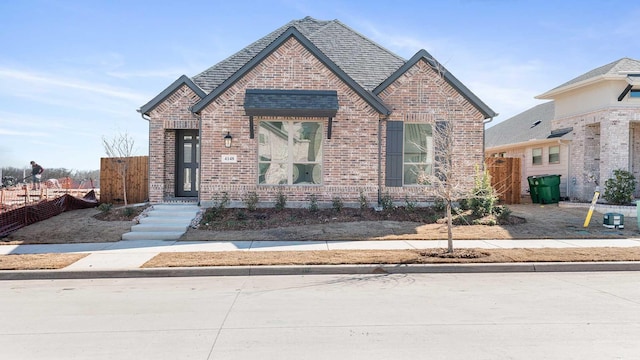 view of front of house with a shingled roof, brick siding, and fence