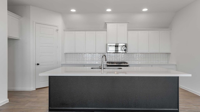 kitchen featuring wood finished floors, a sink, white cabinetry, light countertops, and stainless steel microwave