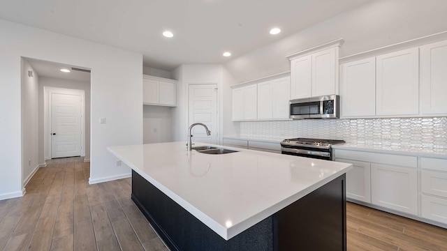 kitchen with a kitchen island with sink, appliances with stainless steel finishes, a sink, and wood finished floors