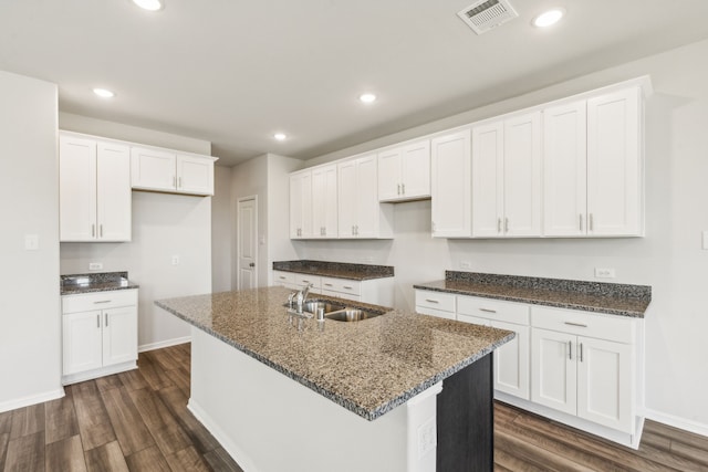 kitchen with white cabinetry, sink, dark hardwood / wood-style flooring, dark stone counters, and a center island with sink