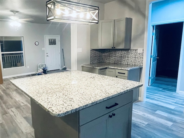 kitchen featuring decorative backsplash, light wood-style flooring, ceiling fan with notable chandelier, and light stone countertops