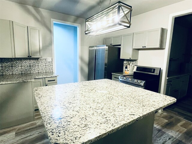 kitchen featuring light stone counters, dark wood-style flooring, stainless steel appliances, decorative backsplash, and a center island