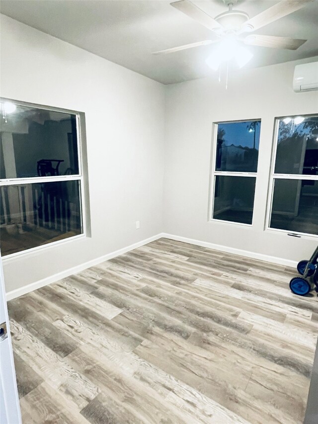 unfurnished room featuring a wall mounted air conditioner, baseboards, wood finished floors, and ceiling fan