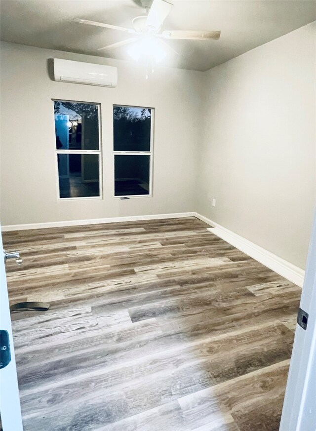 empty room featuring ceiling fan, wood finished floors, baseboards, and a wall mounted AC