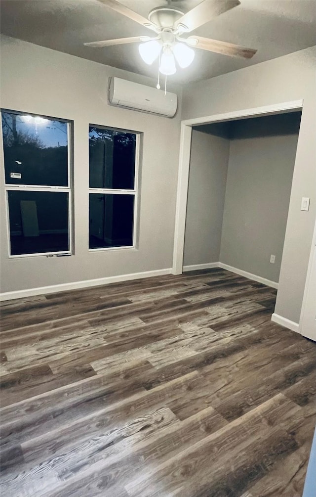 empty room with an AC wall unit, a ceiling fan, baseboards, and wood finished floors