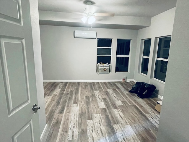 unfurnished room featuring a ceiling fan, an AC wall unit, wood finished floors, and baseboards