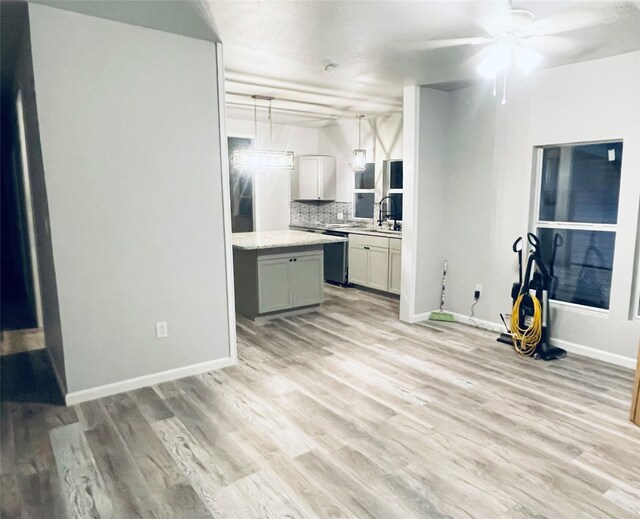 kitchen featuring pendant lighting, light wood-style flooring, a sink, decorative backsplash, and baseboards