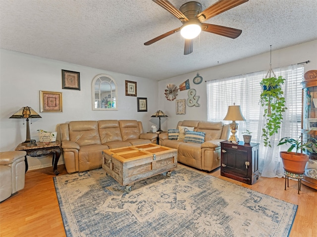 living room featuring ceiling fan, light wood-type flooring, and a textured ceiling