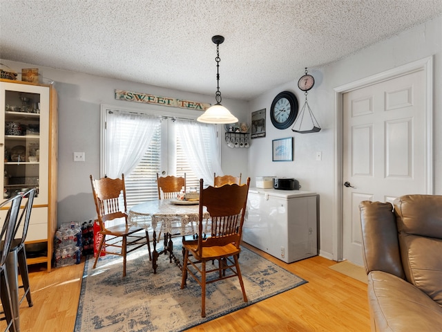 dining space with light wood-type flooring and a textured ceiling