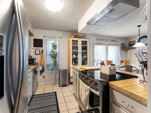 kitchen featuring stainless steel appliances, ventilation hood, plenty of natural light, decorative light fixtures, and light tile patterned floors