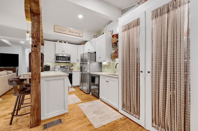 kitchen featuring stainless steel appliances, white cabinetry, light hardwood / wood-style flooring, and decorative backsplash