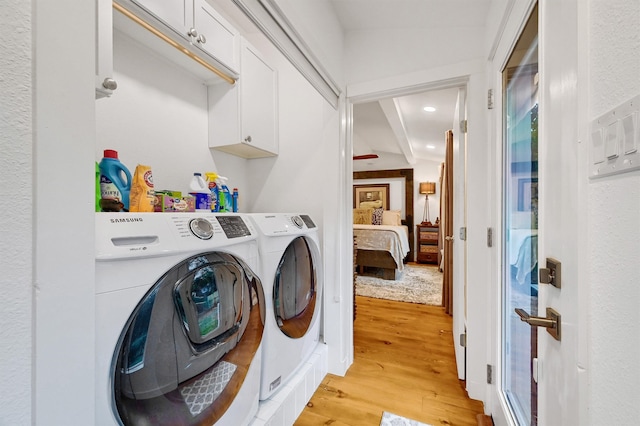 clothes washing area with washing machine and dryer, cabinets, and light hardwood / wood-style flooring