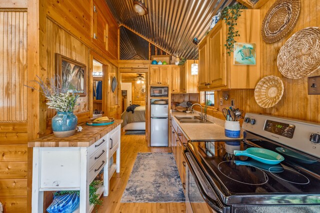 kitchen featuring stainless steel appliances, light wood-type flooring, wood walls, sink, and vaulted ceiling