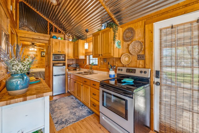 kitchen featuring appliances with stainless steel finishes, decorative light fixtures, wood walls, sink, and lofted ceiling