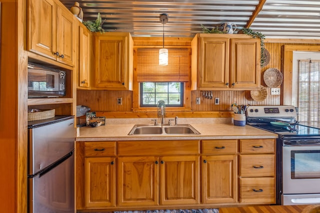 kitchen with sink, appliances with stainless steel finishes, decorative light fixtures, wood-type flooring, and wooden walls