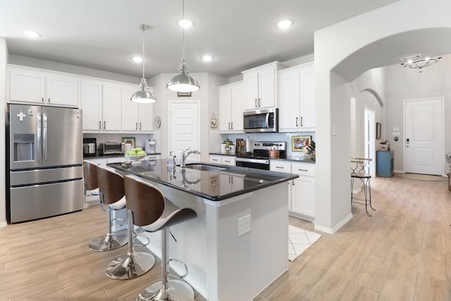 kitchen with stainless steel appliances, a kitchen island with sink, light hardwood / wood-style flooring, white cabinets, and decorative backsplash