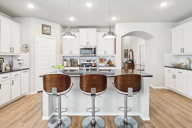 kitchen featuring light wood-type flooring, appliances with stainless steel finishes, tasteful backsplash, and decorative light fixtures