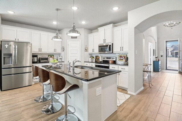 kitchen with stainless steel appliances, white cabinetry, sink, decorative light fixtures, and an island with sink