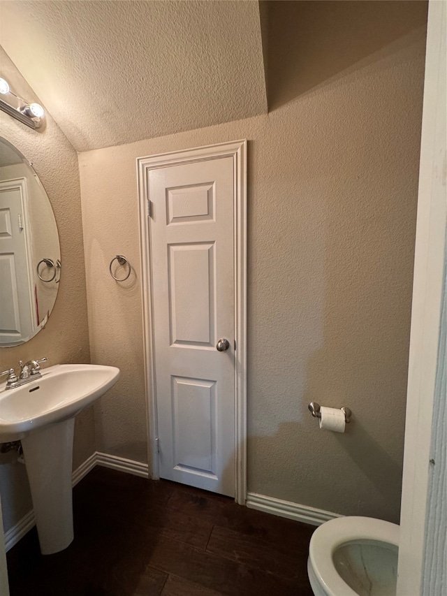 bathroom with toilet, wood-type flooring, sink, and lofted ceiling