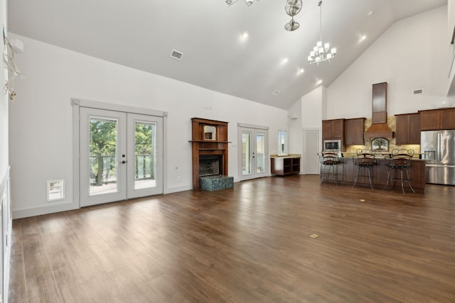 unfurnished living room featuring french doors, a towering ceiling, dark hardwood / wood-style floors, and a notable chandelier