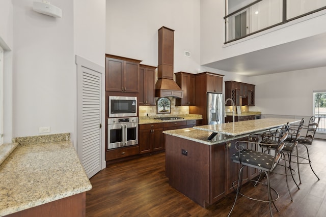 kitchen with custom exhaust hood, a high ceiling, appliances with stainless steel finishes, kitchen peninsula, and a breakfast bar area