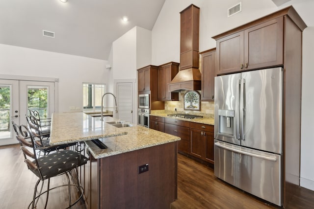 kitchen featuring custom exhaust hood, a kitchen island with sink, french doors, sink, and stainless steel appliances