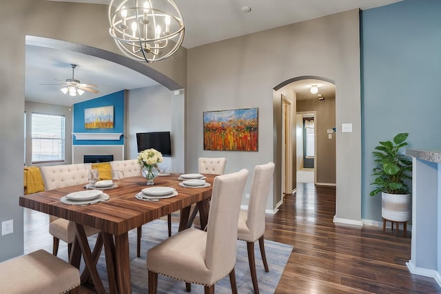 dining space with dark hardwood / wood-style floors, a fireplace, and ceiling fan with notable chandelier