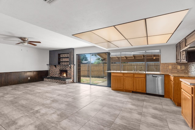 kitchen with wood walls, ceiling fan, a brick fireplace, dishwasher, and decorative backsplash