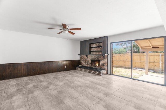 unfurnished living room featuring a fireplace, wood walls, ceiling fan, and lofted ceiling